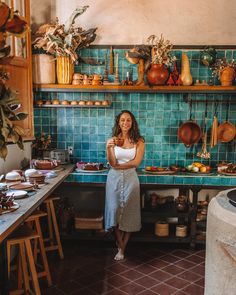 a woman standing in front of a blue tiled wall with pots and pans on it