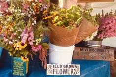 some flowers are sitting on a blue table cloth and there is a sign that says mixed bouquets