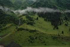 the mountains are covered in clouds and green grass, with a stream running through them