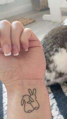 a small tattoo on the wrist of a woman with a cat in the back ground