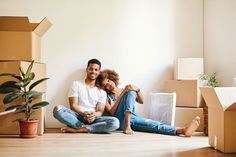 a man and woman sitting on the floor surrounded by moving boxes