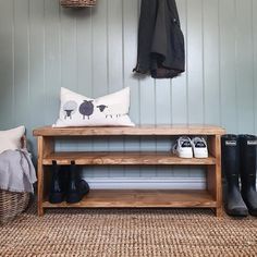 a wooden bench sitting under a coat rack next to a pair of black boots and a white pillow