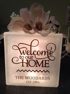 a glass block with the words welcome to our home on it and flowers in front