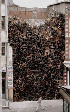 a large pile of wooden chairs sitting on the side of a building next to a street