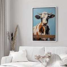 a painting of a cow is hanging on the wall above a white couch in a living room