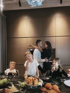 a group of people sitting around a table with cakes and fruit on top of it