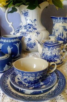 a blue and white china set with flowers in the vase behind it on a lace tablecloth