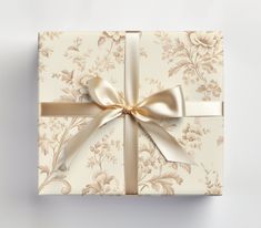 a white gift box with a gold ribbon and bow on the top is decorated with floral wallpaper