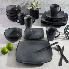 a table set with black dishes and silver utensils, limes and cups