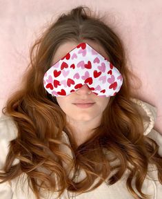 a woman with her eyes closed wearing a heart shaped blindfold over her eye, in front of a pink background