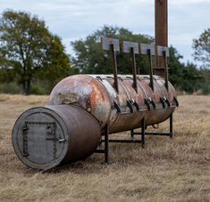 an old metal barrel sitting in the middle of a field with trees in the background