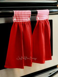 two red kitchen towels hanging from the handle of an oven