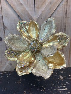 a gold flower with lots of sparkles on it sitting in front of a wooden wall