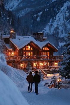 two people standing in front of a ski lodge at night with lights on the windows