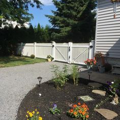 a white picket fence next to a flower bed in front of a house with flowers on the ground