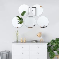 a white dresser topped with lots of mirrors next to a potted plant on top of a wooden shelf