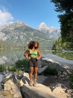 a woman standing on top of a rock next to a lake