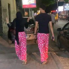 two people are walking down the street in matching pink pants and black shirts with hearts on them