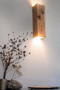 a light that is on the side of a wall next to a vase with flowers