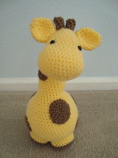 a crocheted stuffed giraffe sitting on the floor next to a wall