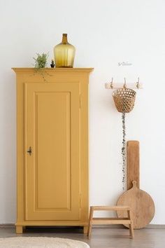 a yellow cabinet sitting next to a wooden chair and vase on top of a shelf