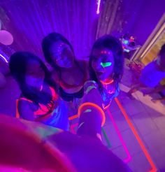 three girls are posing for the camera in front of some neon colored lights and confetti