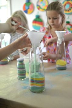 two girls and one girl are making sand in vases with spoons on the table