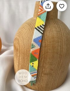 the beaded bracelet is on display in front of a wooden vase and white cloth