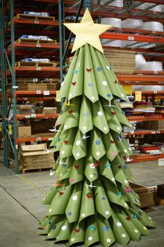 a christmas tree made out of rolled up green paper in a warehouse with shelves and boxes behind it