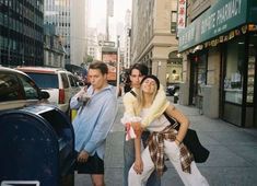 three people standing on the sidewalk in front of cars