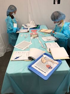 two people in protective clothing are sitting at a table with papers and laptops on it