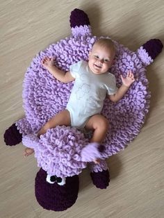 a baby is laying on top of a purple sheep rug that looks like it has been made out of yarn