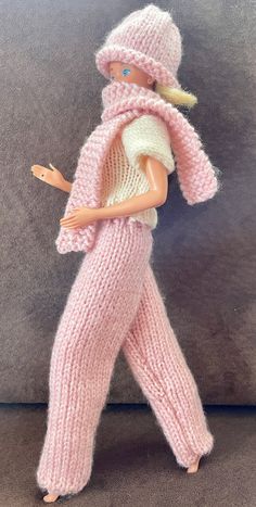 a barbie doll wearing pink knitted clothing and hat with her hand on her hip