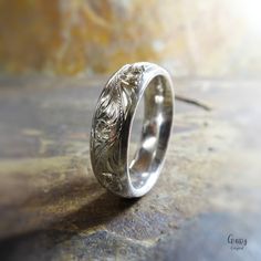 a silver ring with an intricate design on it sitting on a stone surface in the sunlight