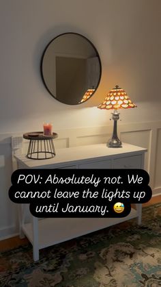 a white table with a lamp on it and a mirror above it that says pov absolutely not we cannot leave the lights up until january