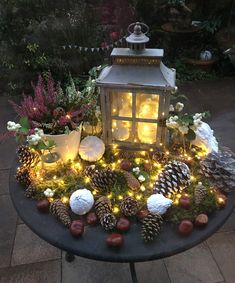 a table topped with lots of pine cones and christmas lights next to a lantern light