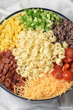 a bowl filled with pasta, cheese, tomatoes and ground beef next to green onions