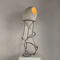 a metal sculpture sitting on top of a white table next to a gray wall with an orange light