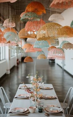 a long table with plates and place settings under colorful umbrellas hanging from the ceiling