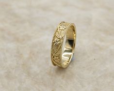 a gold wedding ring with an intricate design on the outside and inside, sitting on a marble surface