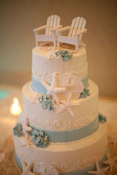 a wedding cake with two chairs and starfishs on the top, decorated in blue and white