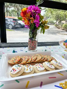 a table topped with lots of cookies and sprinkles next to a vase filled with flowers