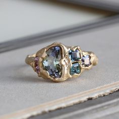 Our handmade tanzanite ring celebrates the unique particolor of this ethically sourced gemstone. An unusual crescent shape weighing 1.35 ct, the glittering ombre hues of green to purple are completely as Mother Nature intended: no-heat treatment for color or clarity with exceptionally energetic sparkle. Natural pink, purple and green spinel and twin pink Malaya garnet accents play to the ethereal and shifting colors of the main stone; the organic vibe is carried through with the textured branch-style band. An easy to wear low profile and measuring approximately 10.55 mm (about 3/8") north to south at the center front with a 2-3 mm average band width.  Currently size 6 3/4 and resizable at least two full sizes without issue. We can replicate the branch-like quality of the band at the sizing Malaya Garnet, Hues Of Green, Branch Ring, Bohemian Bridal, Crescent Shape, Custom Gift Boxes, Tanzanite Ring, Purple And Green, Gemstone Colors