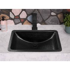 a black sink sitting on top of a white counter next to a potted plant