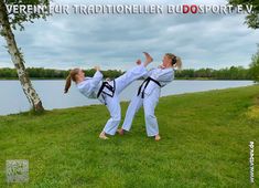 two women are doing karate in front of a body of water with trees behind them