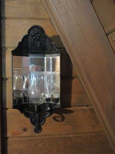 an old fashioned wall mounted light with glasses on it's glass holder and wood paneling