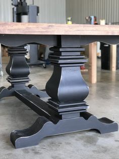 a large table with two black legs and a wooden top in a garage area next to other workbench tools