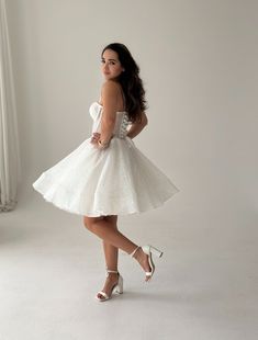 a woman in a short white dress posing for the camera with her hands on her hips