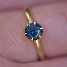 a close up of a person's hand holding a ring with a blue diamond