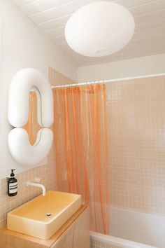 a bathroom with a sink, mirror and bathtub in the corner next to an orange shower curtain